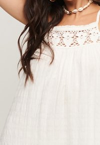 Vestido de verano ligero y blanco con un borde de encaje en el escote, tejido texturizado y un diseño suelto y fluido.