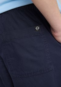 Pantalones cortos azul marino de tela suave, con cintura elástica, bolsillo lateral y una pequeña etiqueta de marca en el bolsillo trasero.