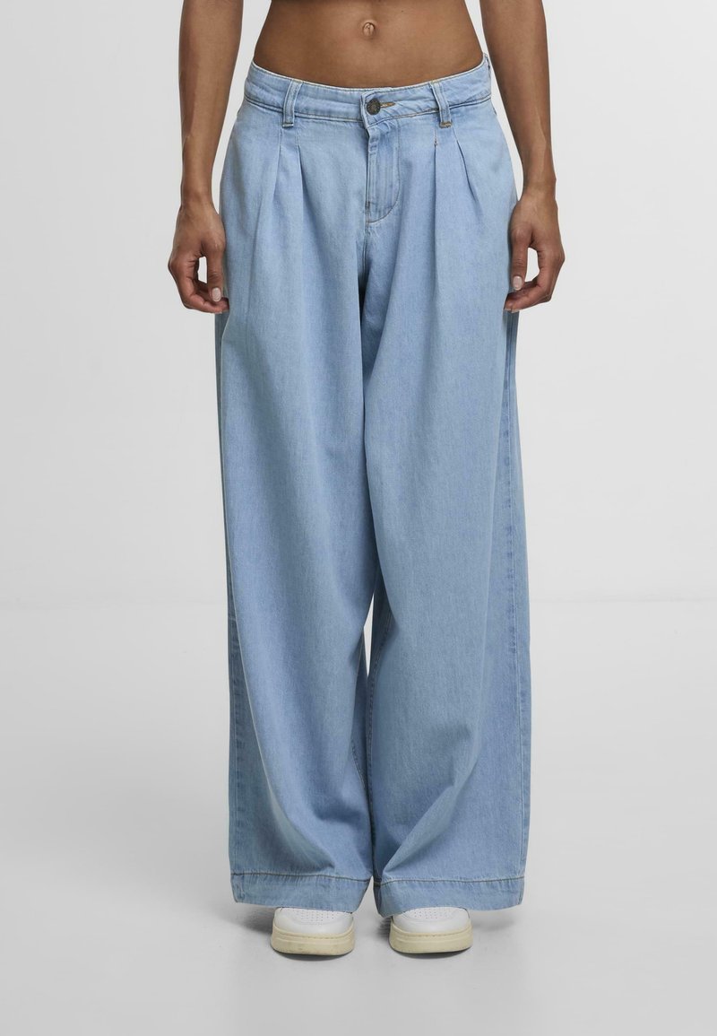 Light blue wide-leg jeans crafted from denim, featuring pleats at the front and a classic button closure. Paired with white sneakers.