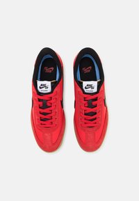Le sneaker Nike SB rosse presentano una tomaia in suede e mesh, dettagli neri e una suola in gomma naturale, con fodera in tessuto e lacci piatti.