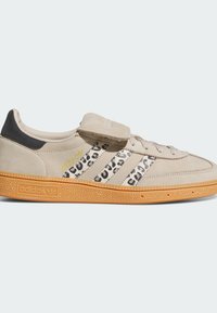 Bež suède tenisice s crnim petama, ukrašene prugama od leopard uzorka i čičak trakama. Gumeni potplat je teksturiran i narančaste boje.