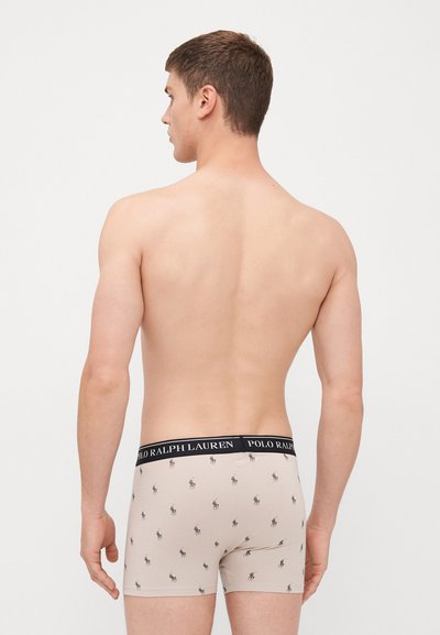Roupa interior bege com um padrão de logotipo escuro repetido, com uma cinta preta que exibe "POLO RALPH LAUREN." Design clássico de boxers.