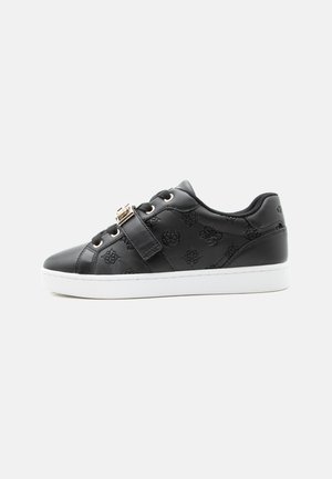 Czarny niskoprofilowy sneaker z wytłaczanymi wzorami, zawiązywany na sznurówki, z ozdobnym paskiem na klamrę i grubą białą gumową podeszwą.
