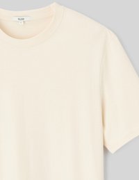 T-shirt beige clair à manches courtes en coton doux, avec un col rond et un design simple sans motifs ni accents visibles.