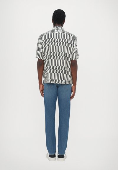 Short-sleeve shirt in black and white geometric pattern, paired with blue straight-leg jeans and white sneakers with black accents.