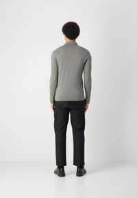 Lange mouw, lichtgrijze top met een opstaand halsje, gecombineerd met zwarte, cargo-stijl broeken. Glad materiaal met een aansluitend ontwerp. Effen oppervlaktes.