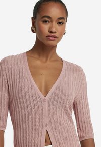 Ljusrosa stickad cardigan med V-ringning, kort ärm, ribbad textur och knäppning med öppen framsida.