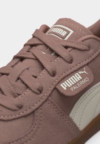 Κοντινό πλάνο του παπουτσιού Puma Palermo σε λιλά σουέντ, με υφασμένες κορδόνια, λευκό λογότυπο Puma και μπεζ λωρίδα στο πλάι σε σόλα από καουτσούκ.