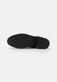 Suela de zapato negra con una superficie de goma texturizada, que presenta un borde suave y curvado y una impresión de logo cerca del área del talón.