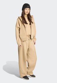 Beige hoodie en bijpassende broek van zacht materiaal, met een oversized pasvorm, drawstring taille en zijzakken. Vergezeld van een zwarte beanie.