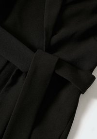 Černý plášť se páskem z texturované tkaniny. Design zahrnuje široké rukávy a měkký spad, který je vhodný pro vrstvení.