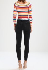 Vaqueros pitillo negros con una textura suave, combinados con una camiseta de manga larga a rayas multicolores, vistos desde atrás. Incluye zapatos de tacón alto.