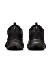 Des chaussures de sport noires avec une tige texturée, un col rembourré et une semelle robuste dotée d'une profonde bande de traction. Logo bien visible au niveau du talon.