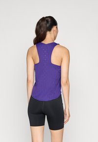 Débardeur violet avec un dos décolleté, présentant une surface texturée et de légers trous de ventilation. Associé à un short noir ajusté.