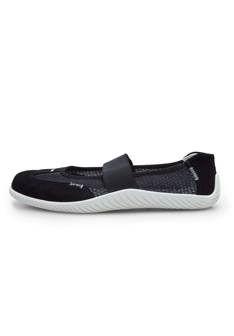 Zapato negro sin cordones con parte superior de malla, suela de goma blanca en contraste y una correa elástica decorativa. Presenta un diseño de punta redondeada.