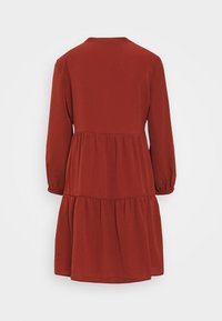 Robe rouge à manches longues avec un col rond, jupe à volants et poignets élastiques. Fabriquée en tissu doux avec une coupe décontractée.