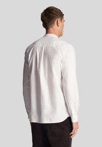 Camicia bianca a maniche lunghe realizzata in cotone morbido, con collo classico e polsini con bottoni, orlo curvo e dettagli di cuciture minime.