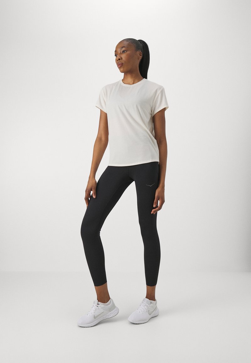 T-shirt beige chiaro a maniche corte abbinato a leggings neri e scarpe da ginnastica bianche. La maglietta presenta una vestibilità rilassata e un colletto rotondo.