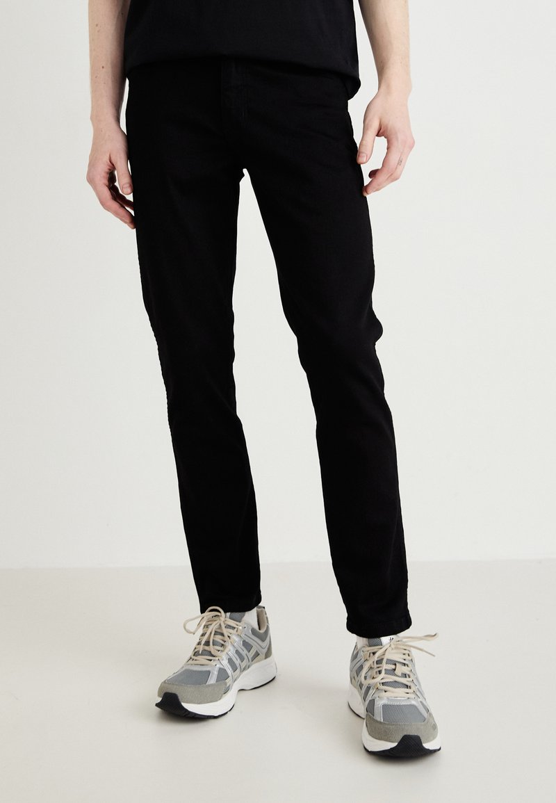 Vaqueros negros ajustados con una textura suave, combinados con zapatillas deportivas grises y blancas que cuentan con cordones y detalles de malla.