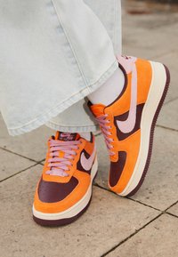 Nike Air Force 1-sneakers med orange mocka och bruna läderpaneler, rosa accenter och en texturerad gummisula med snörning.