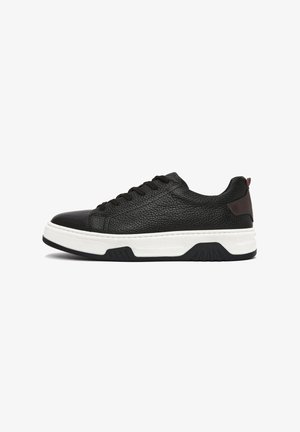 Black leather sneakers with textured surface, white rubber sole, and black accents. Features lace closure and brown heel detail.