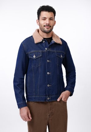 Chaqueta de denim en azul oscuro con cuello de sherpa beige, cierre frontal de botones, dos bolsillos en el pecho y puños abotonados. Textura suave y diseño clásico.