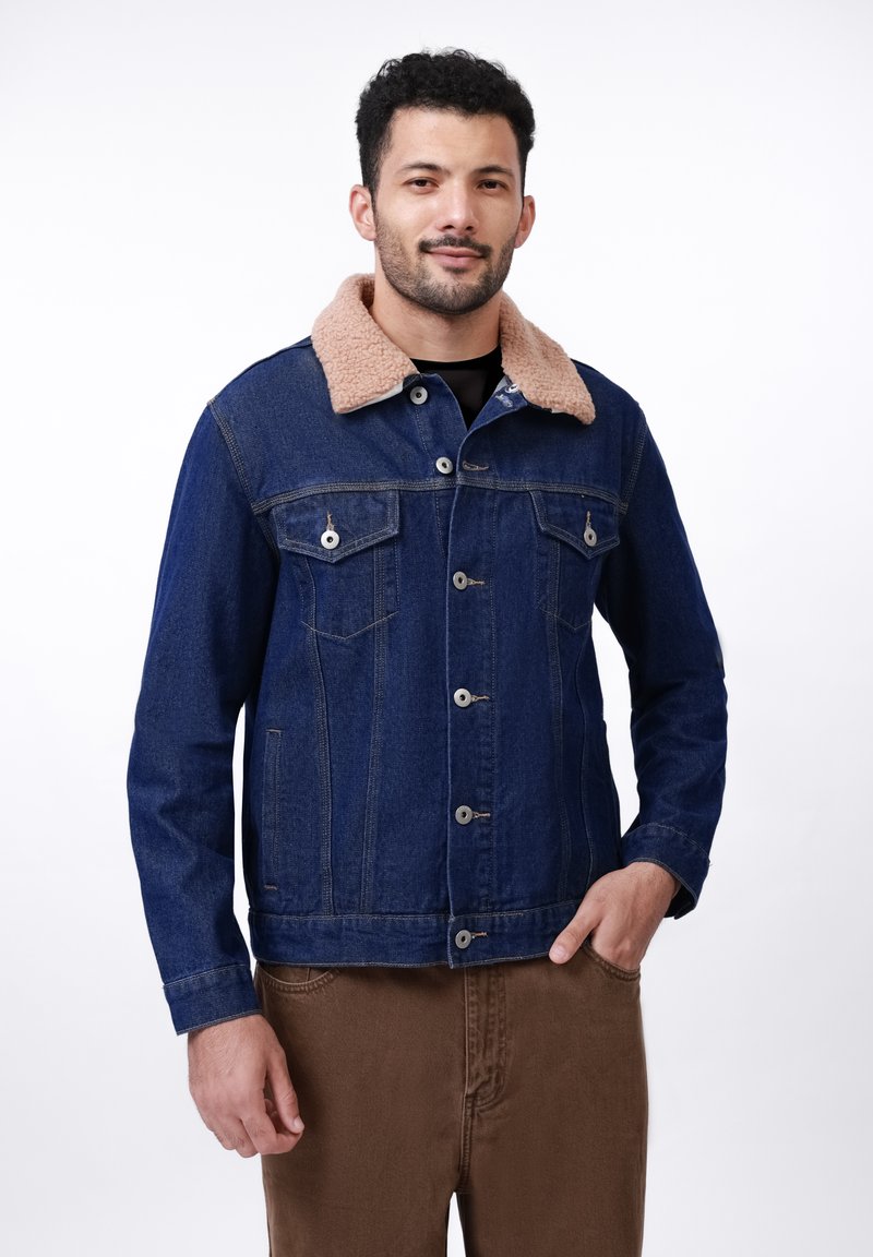 Chaqueta de denim en azul oscuro con cuello de sherpa beige, cierre frontal de botones, dos bolsillos en el pecho y puños abotonados. Textura suave y diseño clásico.