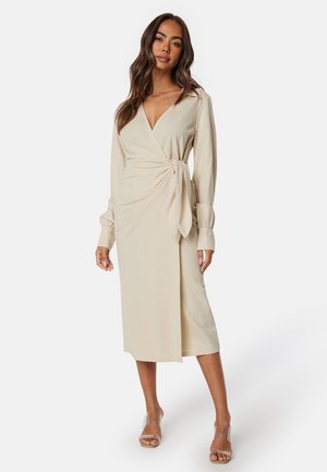 Beige omslagsklänning med långa ärmar, ett band i midjan och längd till mitten av vaden. Slät tyg med en mjuk textur och v-ringad design.