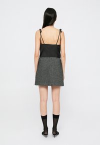 Svart topp med tynne stropper, kombinert med et grått tweedskjørt. Skjørtet har en markert kant og teksturkontrast, og bæres med svarte sokker og hæler.