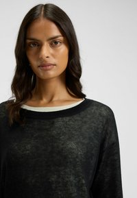 Black knit sweater with a subtle texture, featuring a wide neckline with a contrasting cream-colored trim. Long sleeves, relaxed fit.