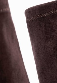 Brązowa tkanina zamszowa o miękkiej fakturze, z czystym szwem wzdłuż górnej krawędzi. Obraz skupia się na materiale i kroju.