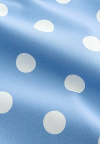Tissu bleu clair avec de grands pois blancs, montrant des plis doux et une texture lisse.