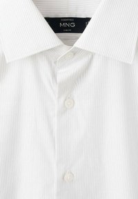 Witte slim-fit shirt met subtiele verticale strepen, puntige kraag en vijf knopen. De stof heeft een gladde textuur; label zichtbaar aan de binnenkant van de kraag.