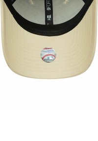 Cappellino da baseball beige con visiera nera, dotato di un adesivo circolare del logo MLB centrato sul rovescio della visiera. Tessuto testurizzato.
