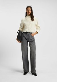 Off-white värjätty turtleneck-neule, harmaat leveälahkeiset farkut, musta vyö, mustassa käsilaukussa, mustat kärkitossut.