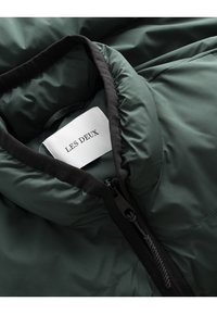 Green insulated jacket with a high collar, zip closure, and soft inner lining. Branding label prominently displayed.