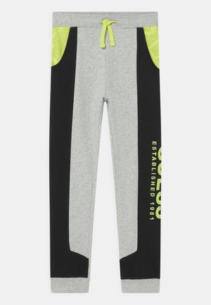 Jogging gris avec panneaux latéraux noirs et poches jaunes, doté d’un cordon jaune et du texte jaune "ESTABLISHED 1981" sur la jambe droite.