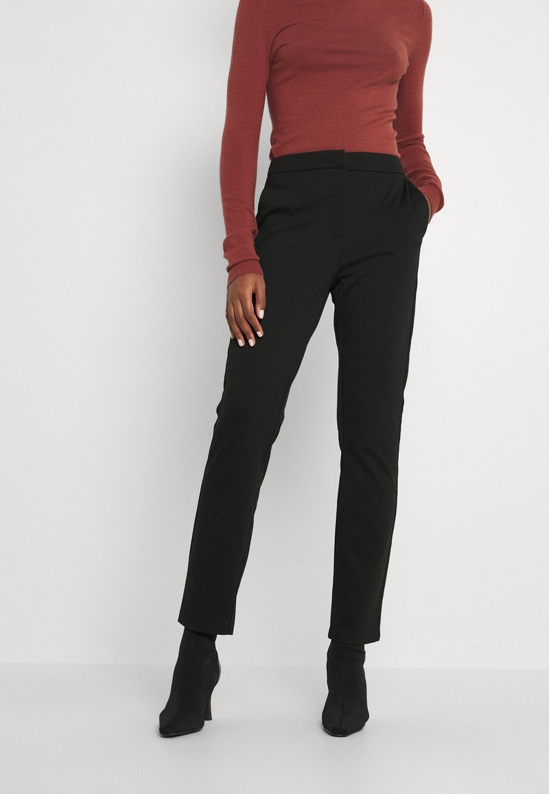 Mustat räätälöidyt housut, joissa on jämäkkä leikkaus, yhdistetty istuvaan viininpunaiseen pitkähihainen paitaan. Sileä kangas, jossa on hienovarainen kiilto, nilkkapituiset.