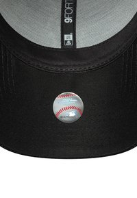 Crna bejzbol kapa s glatkim, strukturiranim dizajnom. Ima okruglu MLB naljepnicu s grafikom bejzbola na donjoj strani vizira.