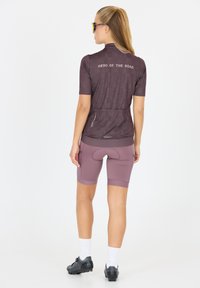 Maillot de cyclisme à manches courtes en violet foncé avec un motif à pois et le texte "HÉROS DE LA ROUTE" au dos ; associé à un short de vélo assorti.