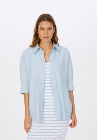 Hellblaues, übergroßes Hemd mit Knöpfen, klassischem Kragen und Brusttaschen, getragen über einem weiß-blauen gestreiften Tankkleid.