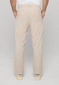 Pantalon beige à coupe décontractée avec une taille élastique, doté de deux poches arrière et d'une texture lisse, associé à des baskets de couleur claire.