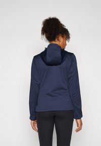 Giacca leggera di colore blu navy con cappuccio e maniche lunghe. Presenta una texture liscia e cuciture a contrasto lungo i lati.