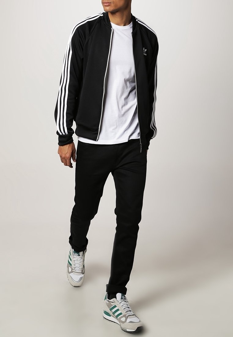Black track jacket with white three-stripe design, white t-shirt, black pants, and gray sneakers with green accents.