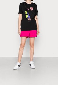 Black graphic t-shirt with colorful print, paired with bright pink shorts. White sneakers with black accents complete the outfit.