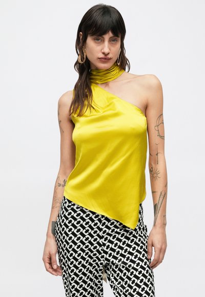 Asymetrický jednoramenný top z jasne žltého saténu s prekladaným golierom a hladkou textúrou, skombinovaný s čiernobielymi vzorovanými nohavicami.