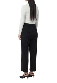 Top bianco a maniche lunghe con dettagli a bottoni e pantaloni neri a gamba larga; tessuto morbido e vita aderente; abbinato a scarpe slingback nere con punta.