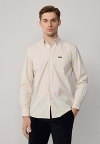 Beige overhemd met lange mouwen en een knoopsluiting-kraag, borstzak en klein logo-label. Katoenen stof met een soepele textuur. Draag met donkere broek.