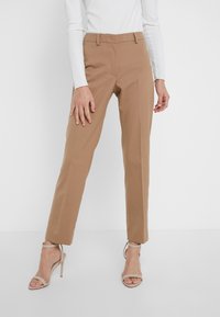 Pantalons taillés couleur beige avec une coupe droite, dotés de poches avant et d'une finition lisse. Assortis à des sandales à talons hauts à lanières de couleur nude.