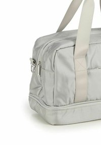 Sac de sport en tissu gris avec une texture en relief diagonale, deux poignées supérieures et une poche zippée sur le côté. Forme compacte et rectangulaire.